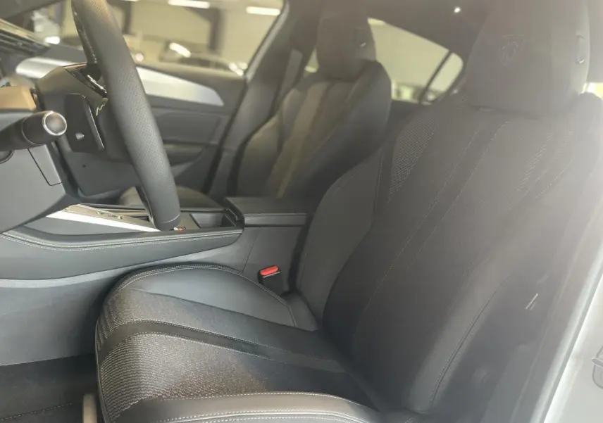 Intérieur de la Peugeot 308 GT 2025 en blanc, vue côté gauche sur les sièges avant en tissu et cuir avec logo Lion brodé.