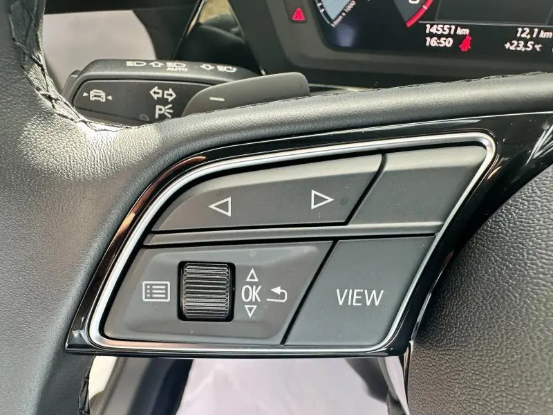 Gros plan sur les commandes au volant noir de l'Audi A3 Sportback 30 TFSI 116ch Hybride blanc Arkona 2024.