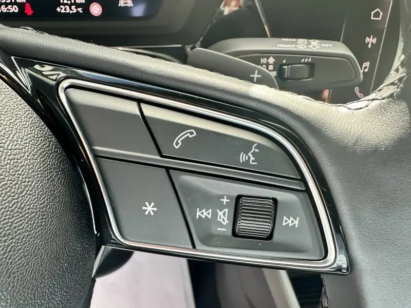 Gros plan sur les commandes vocales et audio au volant cuir de l'Audi A3 Sportback 2024 Hybride, côté gauche.