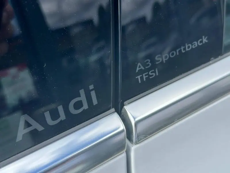 Gros plan sur les inscriptions Audi et A3 Sportback TFSI sur une portière blanche Arkona du modèle 2024.