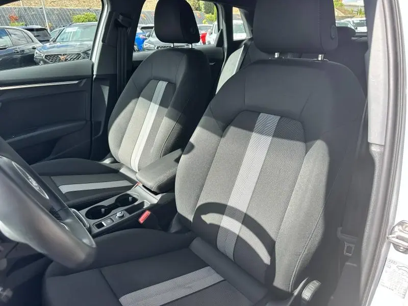 Intérieur de l'Audi A3 Sportback 2024 blanc Arkona, vue côté gauche sur sièges tissu noir avec bandes grises centrales.