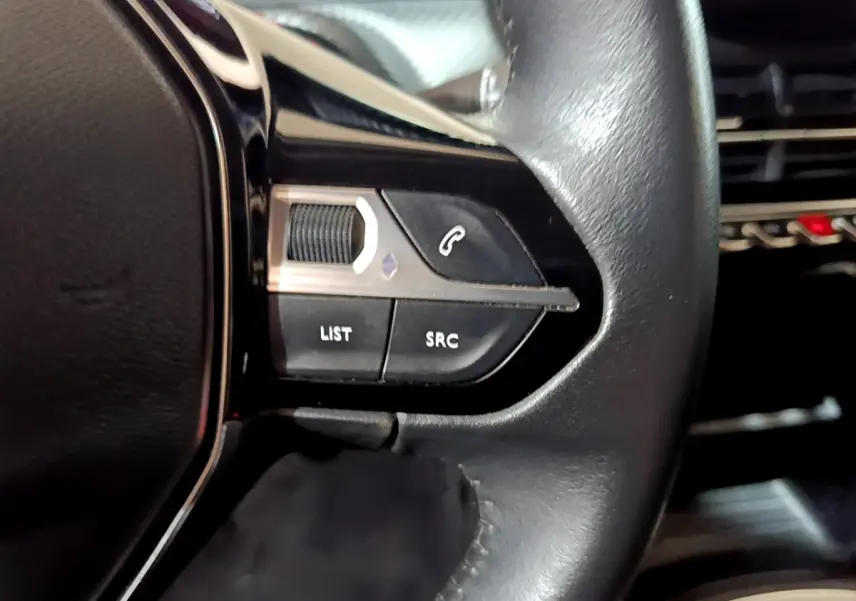 Gros plan sur les commandes gauche du volant cuir noir du Peugeot 2008 gris clair, montrant les boutons de téléphone et audio.