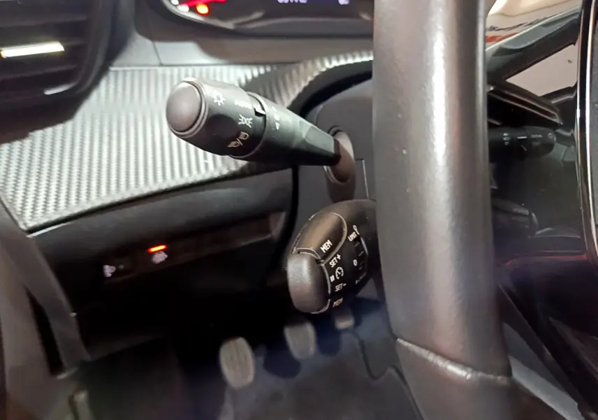 Gros plan sur la commande de régulateur de vitesse et la manette d'éclairage du Peugeot 2008 gris clair, côté conducteur.