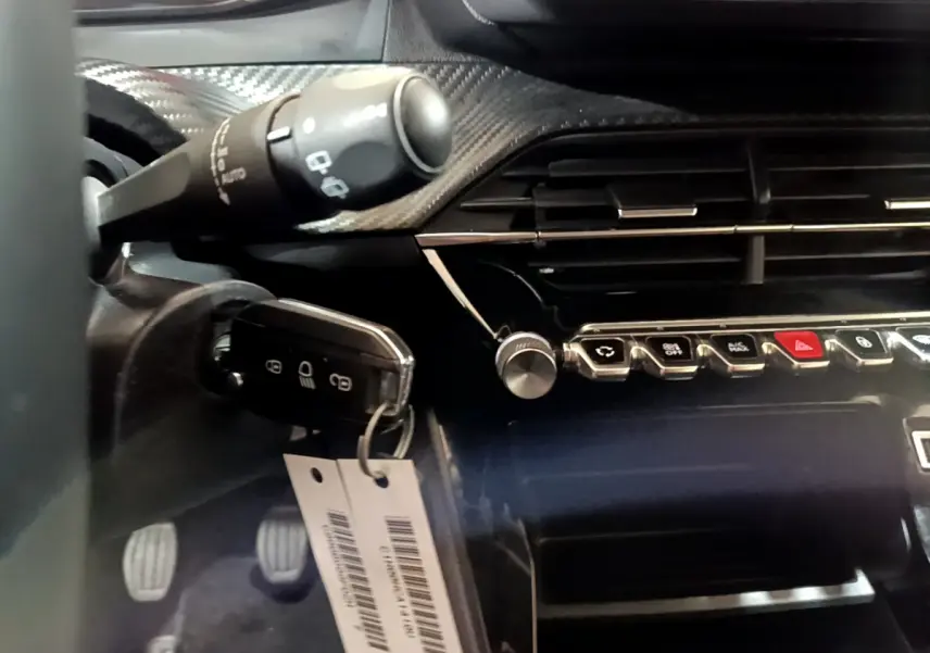 Gros plan sur la clé et la console centrale noire brillante du Peugeot 2008 gris clair, avec commandes et aérateurs visibles.