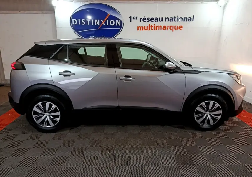 Profil droit d'un Peugeot 2008 gris clair 2022 dans un showroom avec logo Distinxion en arrière-plan.