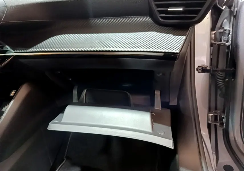 Vue intérieure côté passager du Peugeot 2008 gris clair 2022, boîte à gants ouverte sous tableau de bord noir à insert carbone.