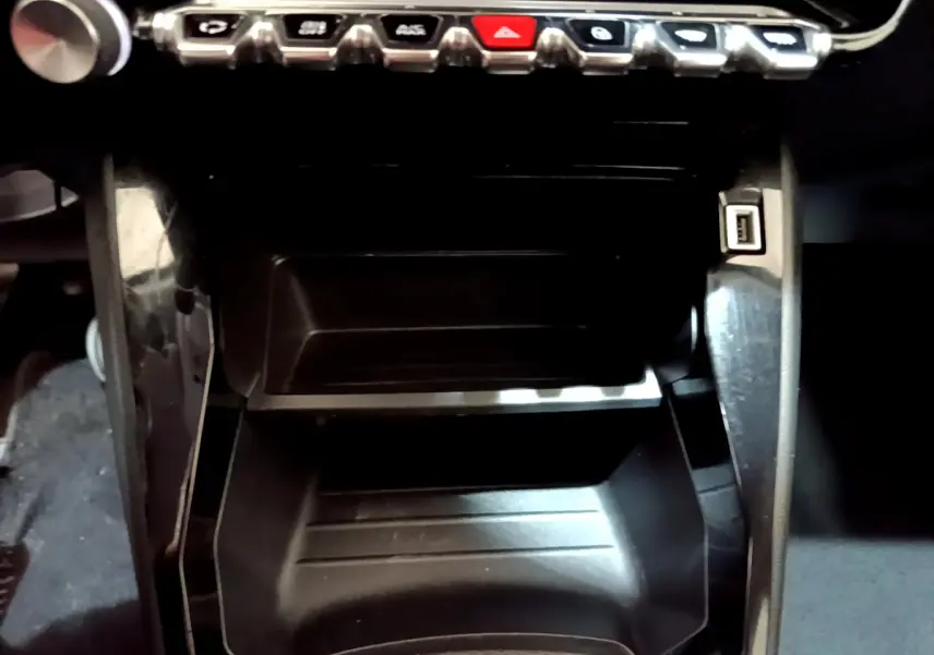 Gros plan sur la console centrale noire d'une Peugeot 2008 gris clair, avec rangements et port USB visible à droite.