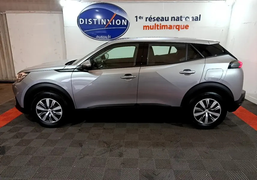 Profil côté gauche d'un Peugeot 2008 BlueHDi 110 S&S Active gris clair, en intérieur sur sol à damier noir et rouge.