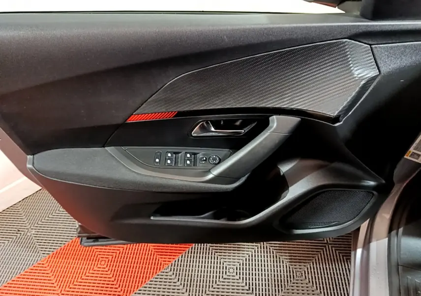 Intérieur côté gauche de la porte avant d'une Peugeot 2008 gris clair, avec commandes électriques et insert décoratif noir.