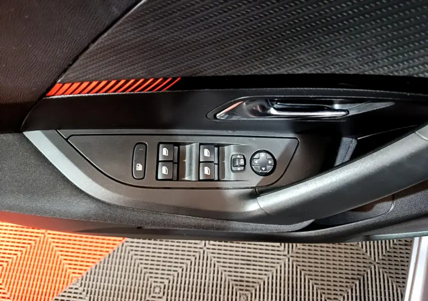 Gros plan sur la commande des vitres et rétroviseurs côté conducteur du Peugeot 2008 gris clair, intérieur noir.