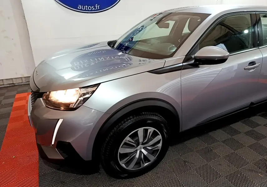 PEUGEOT 2008 gris clair vue 3/4 avant gauche avec phares allumés et jantes alliage distinctives.