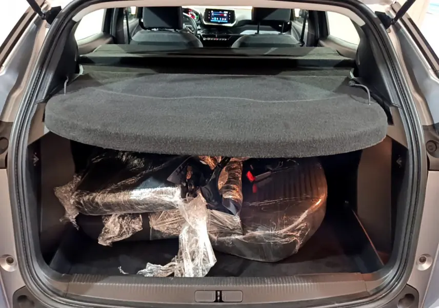 Coffre ouvert d’un Peugeot 2008 gris clair 2022, vue arrière montrant la tablette et un chargement emballé.