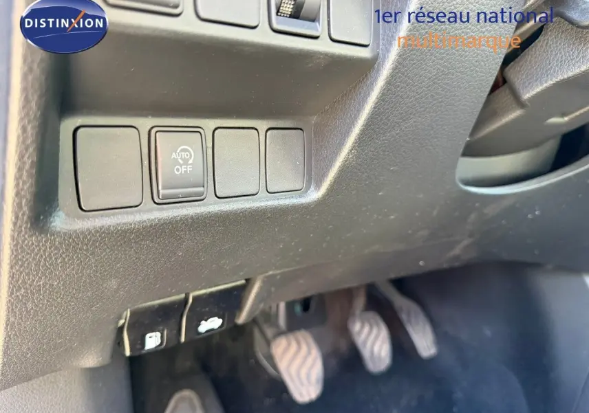 Gros plan sur les commandes sous le tableau de bord côté gauche d’un Nissan Qashqai blanc nacré, pédales visibles.