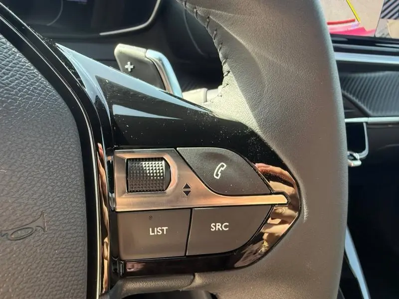 Gros plan sur les commandes au volant côté gauche du Peugeot 2008 Rouge Elixir, avec molette et boutons d’appel et multimédia.
