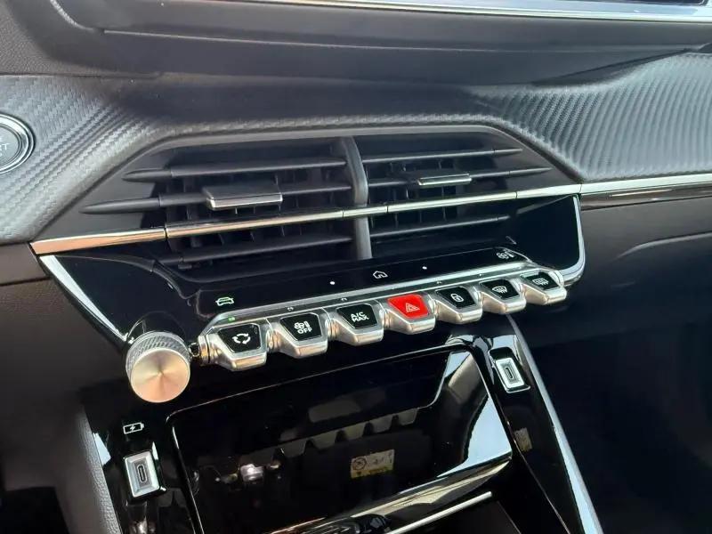 Vue rapprochée de la console centrale du Peugeot 2008 2025, boutons métalliques et finition carbone noire visibles.