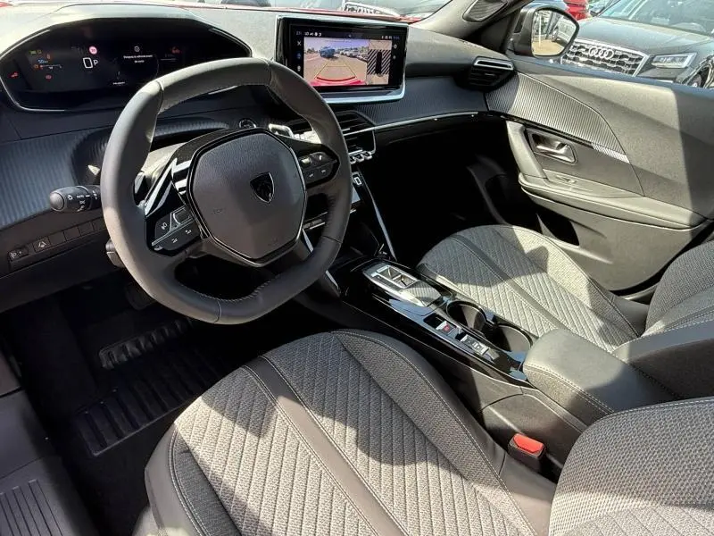 Intérieur de la Peugeot 2008 1.2 Hybrid 145ch Allure 2025, vue côté conducteur, tableau de bord moderne et sièges gris texturés.