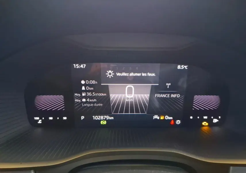 Tableau de bord numérique du Skoda Kodiaq gris clair, affichant la vitesse à 0 km/h et une alerte pour allumer les feux.