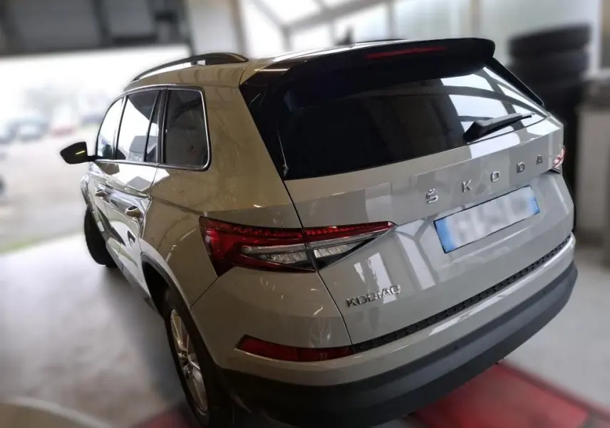 Vue 3/4 arrière droite d'un Skoda Kodiaq gris clair 2023 avec feux arrière LED et toit noir brillant.