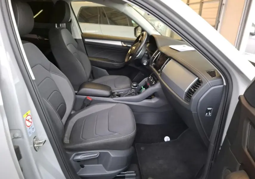 Intérieur avant du Skoda Kodiaq gris clair 2023, vue côté gauche montrant sièges tissu noirs et tableau de bord moderne.