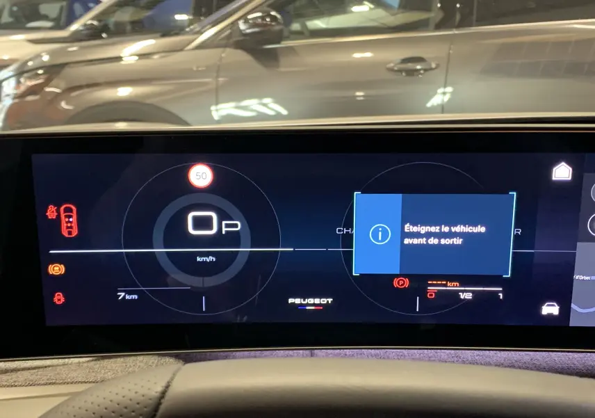 Affichage numérique du tableau de bord du Peugeot 3008 Hybrid, vue frontale, avec message d’alerte et voiture grise en arrière-plan.