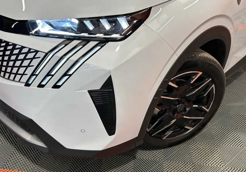 Gros plan sur l'avant droit blanc Okenite du Peugeot 3008 III Hybrid, mettant en valeur les phares LED et la jante noire brillante.