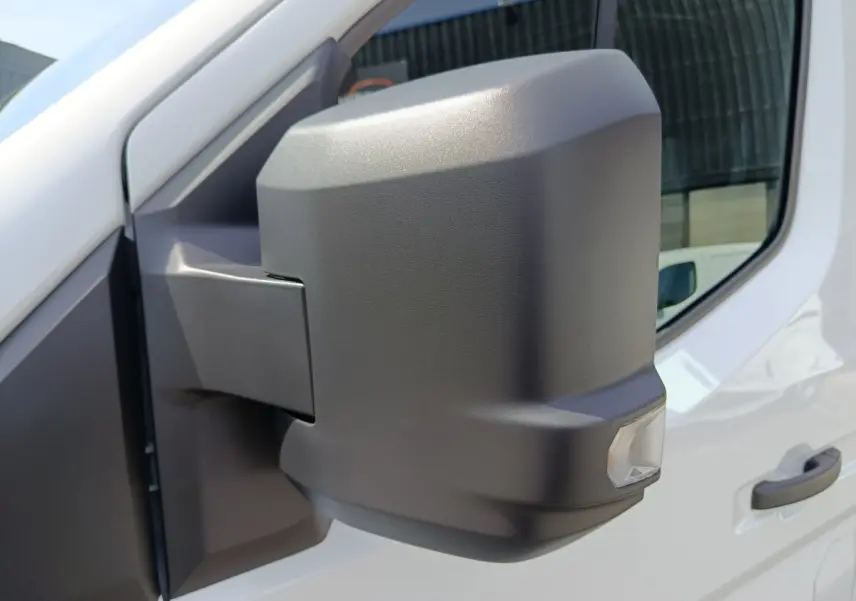 Rétroviseur droit noir en gros plan sur Renault Master blanc, avec porte et fenêtre visibles en arrière-plan.