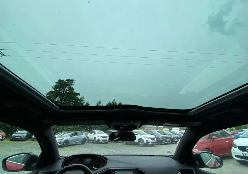 Vue intérieure avant du toit panoramique en verre de la Peugeot 308 GTi rouge avec tableau de bord et rétroviseur central visibles.