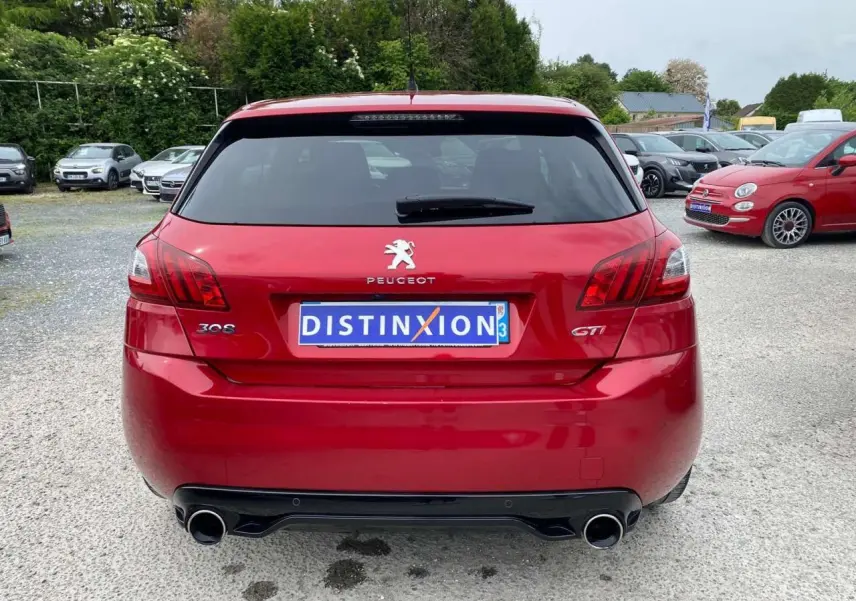 Vue arrière d'une Peugeot 308 GTi rouge métallisée avec double sortie d'échappement et vitre arrière teintée.