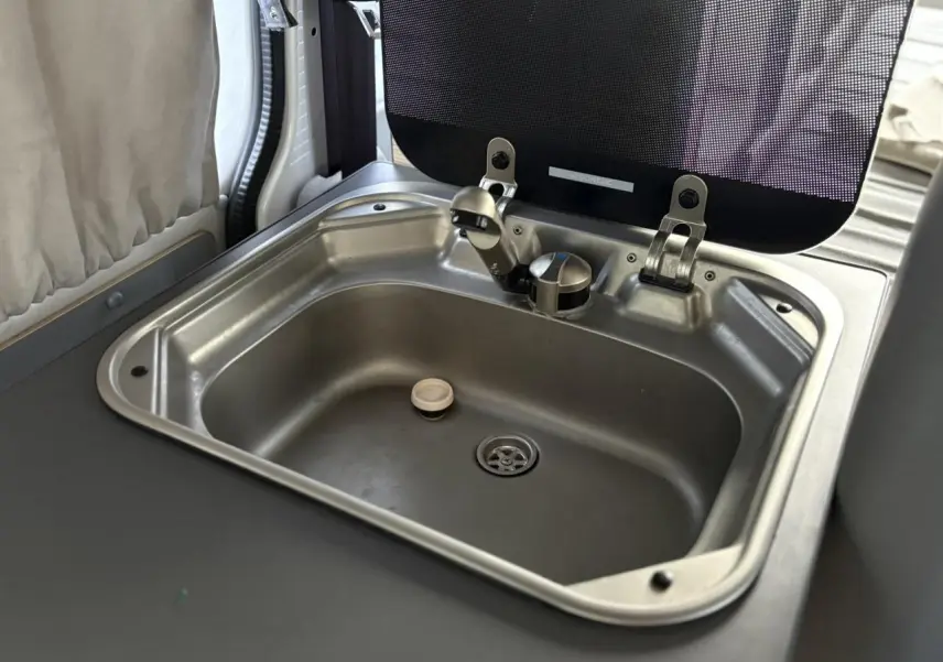 Gros plan sur l'évier en inox intégré dans l'aménagement intérieur du Volkswagen Transporter jaune et blanc.