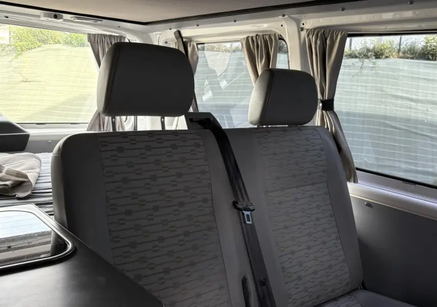 Vue intérieure du Volkswagen Transporter aménagé 2017, montrant les sièges arrière gris avec appuie-têtes et rideaux aux fenêtres.
