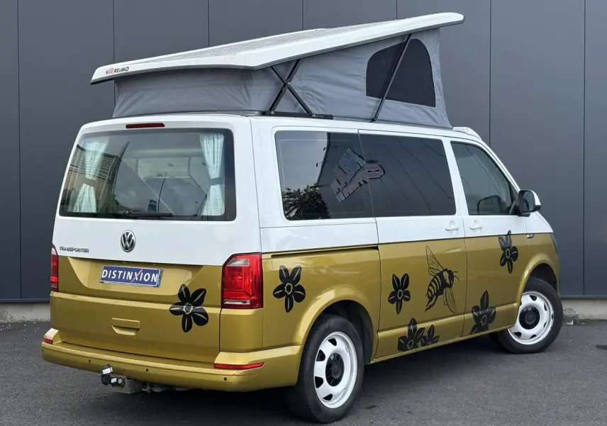 Vue 3/4 arrière droite du Volkswagen Transporter 2017 jaune et blanc avec toit relevé et décor floral noir sur la carrosserie.