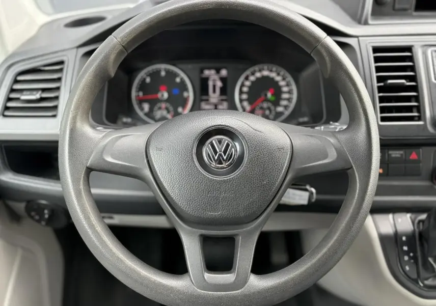 Volant noir avec logo Volkswagen au centre, tableau de bord et commandes du Volkswagen Transporter 2017 visibles en plan rapproché.