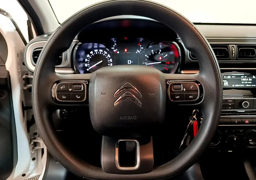 Vue centrée sur le volant noir de la Citroën C3 blanche, avec tableau de bord et commandes au volant visibles.