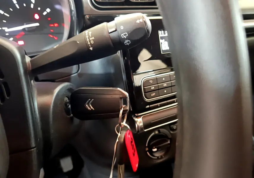 Vue rapprochée de l’intérieur côté gauche du volant noir d’une Citroën C3 blanche avec clé insérée et commandes au tableau de bord.