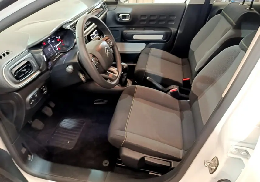 Vue intérieure côté conducteur de la Citroën C3 blanche 2018, sièges noirs et tableau de bord avec volant multifonctions.