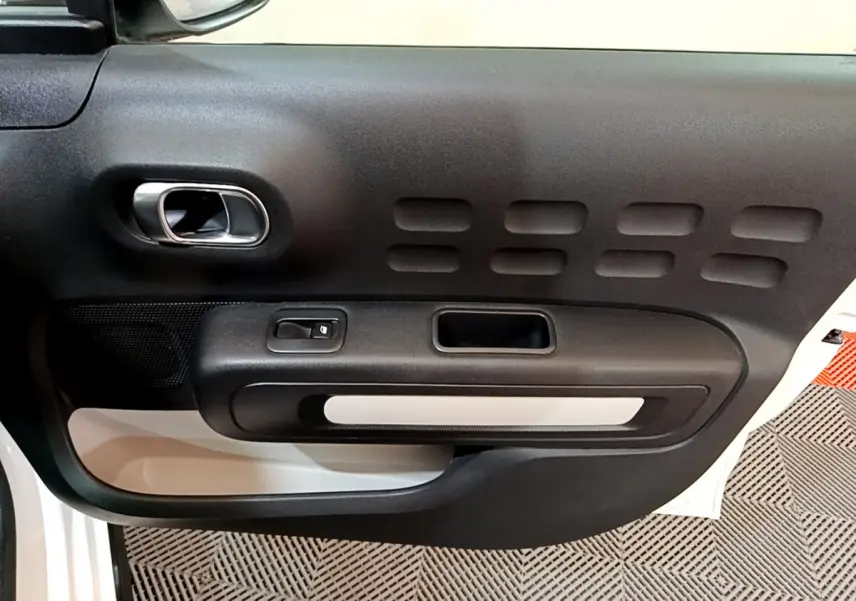 Vue rapprochée de la porte intérieure côté gauche blanche d'une Citroën C3 2018 avec poignée chromée et panneau noir texturé.