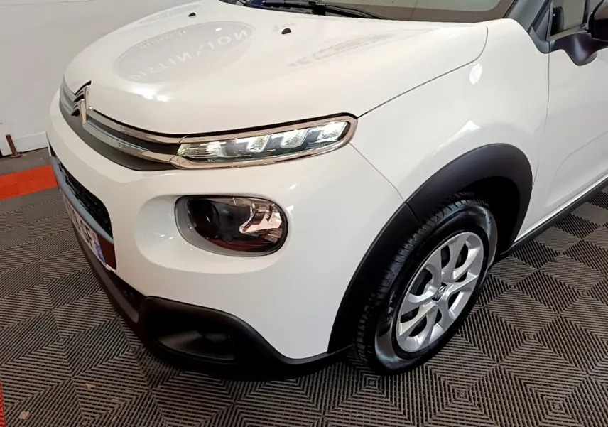 Vue 3/4 avant droit d'une Citroën C3 blanche de 2018 avec phares LED et protections noires sur les ailes.