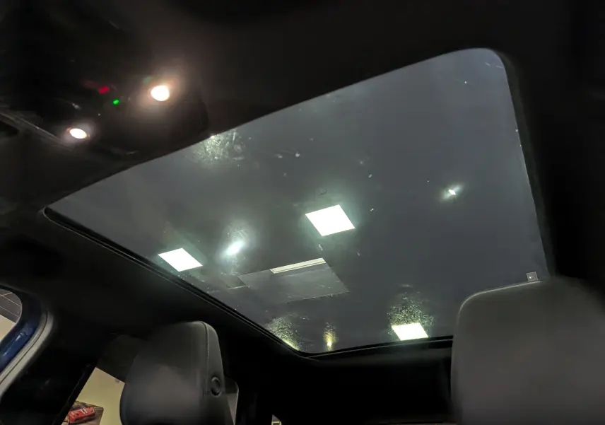 Toit panoramique en verre vu de l'intérieur arrière du Renault Austral E-Tech Hybrid 2024 Bleu Iron avec sièges noirs.