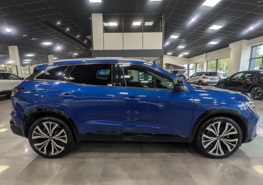 Vue latérale droite du Renault Austral E-Tech Hybrid 200 ch Iconic en Bleu Iron, avec jantes bi-ton et toit noir en showroom.