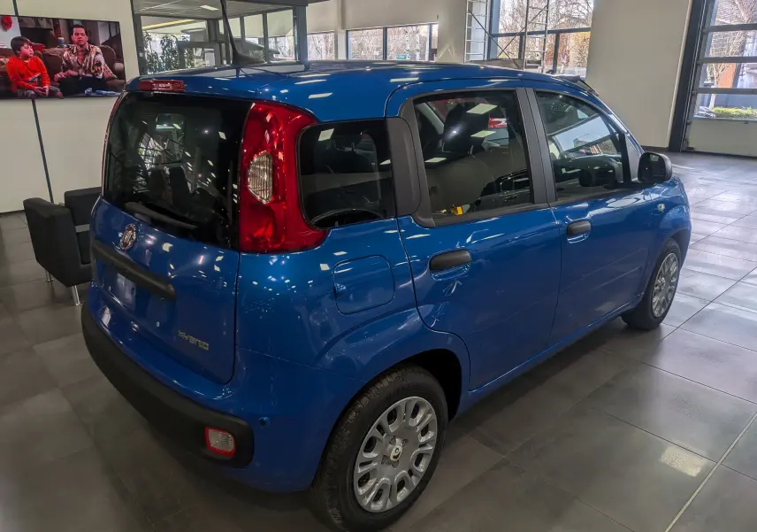Vue 3/4 arrière droite d'une Fiat Panda 1.0 Hybrid City bleu Italia en showroom avec ses feux arrière rouges distinctifs.