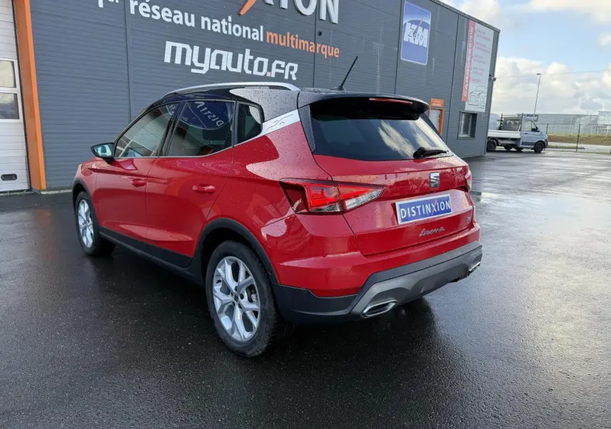 Vue 3/4 arrière droite d'un SEAT Arona Rouge Pur 2024 avec toit noir et jantes argentées sur sol mouillé.