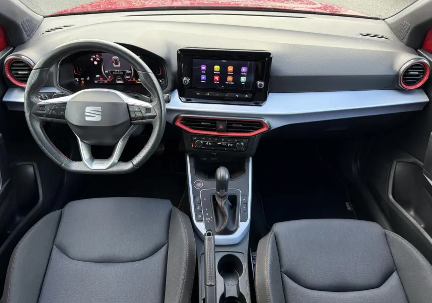 Vue intérieure frontale du tableau de bord du SEAT Arona rouge pur 2024 avec volant sport cuir Nappa et écran tactile central.