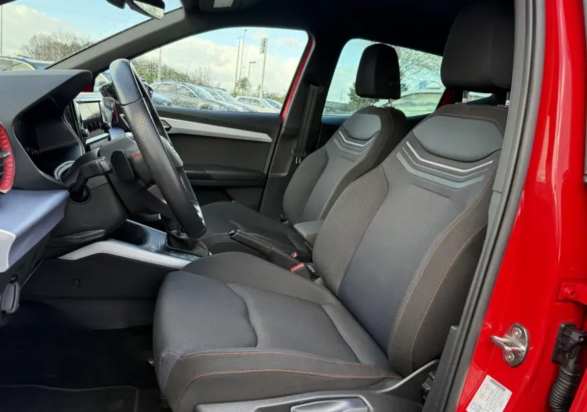 Intérieur avant du SEAT Arona rouge pur 2024, vue côté conducteur, sièges noirs avec surpiqûres rouges et volant sport en cuir.