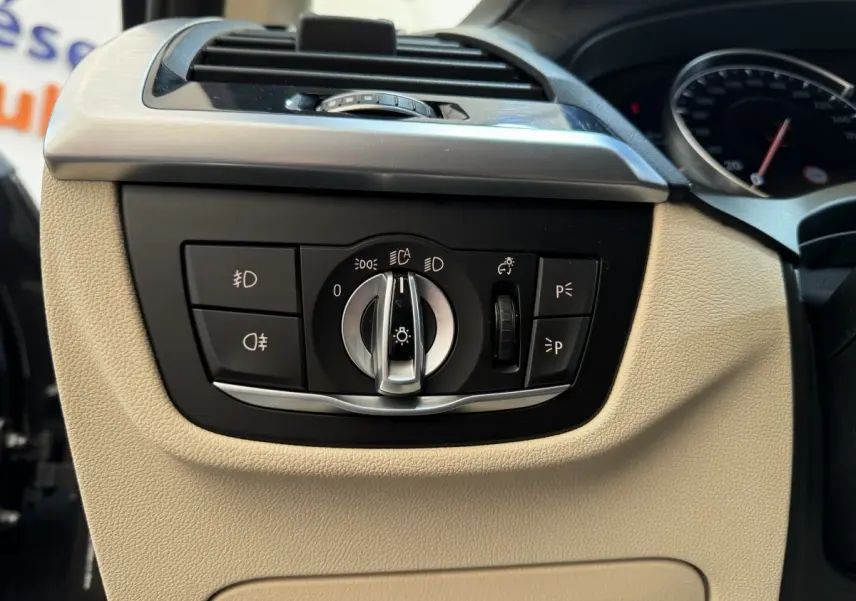 Détail du tableau de bord beige avec commande des phares et ventilation sur BMW X3 xDrive30d gris foncé, vue intérieure côté gauche.