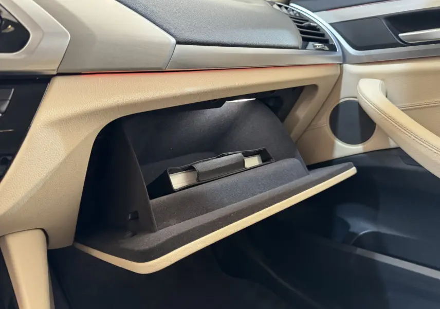 Intérieur beige clair du BMW X3 2018, vue côté passager sur la boîte à gants ouverte avec manuel visible.