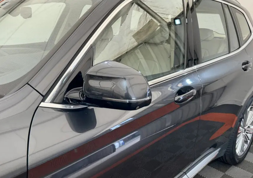 Vue rapprochée côté gauche d’un BMW X3 gris foncé 2018 avec rétroviseur et poignée de porte visibles.