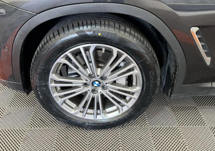 Gros plan sur la roue avant gauche d’un BMW X3 gris foncé avec jante alliage multi-branches et logo BMW visible.