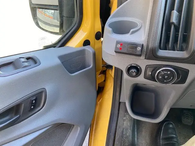 Détail de l'intérieur côté conducteur du Ford Transit jaune, montrant la portière ouverte et les commandes du tableau de bord.
