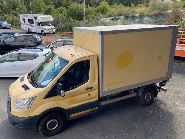 Vue 3/4 avant gauche d'un Ford Transit Chassis Cabine jaune avec caisse fermée et hayon, stationné en extérieur.