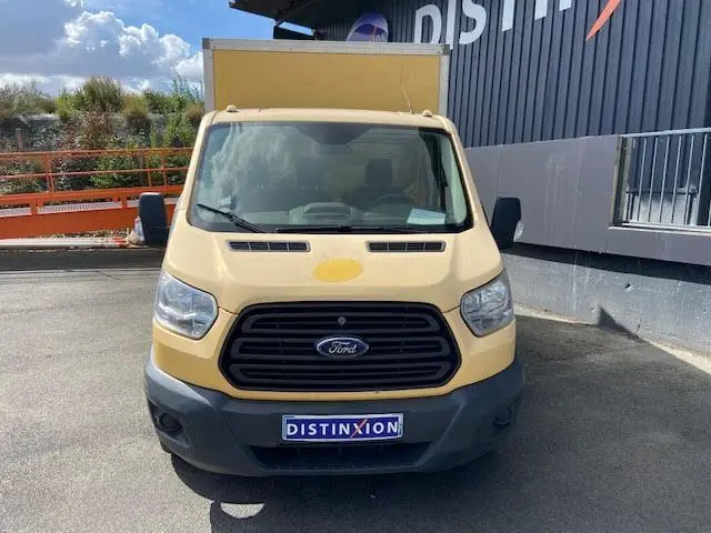 Vue de face d'un Ford Transit Chassis Cabine jaune avec hayon, immatriculé et stationné devant un bâtiment noir.